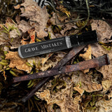 trial vial of grave mistakes fragrance on a background of moss and 2 rusted coffin nails