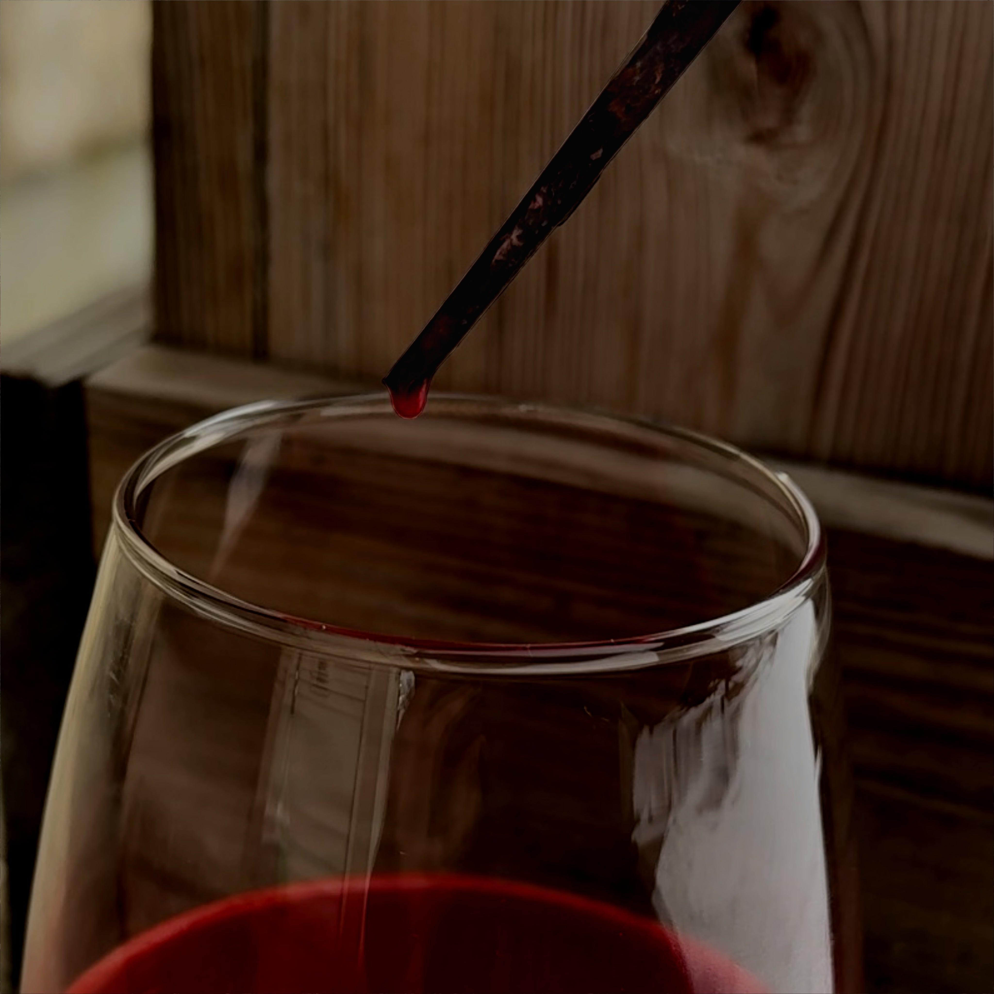 wine glass against wood background. above wine glass is a rusted coffin nail with a drop of blood/wine dripping off of it